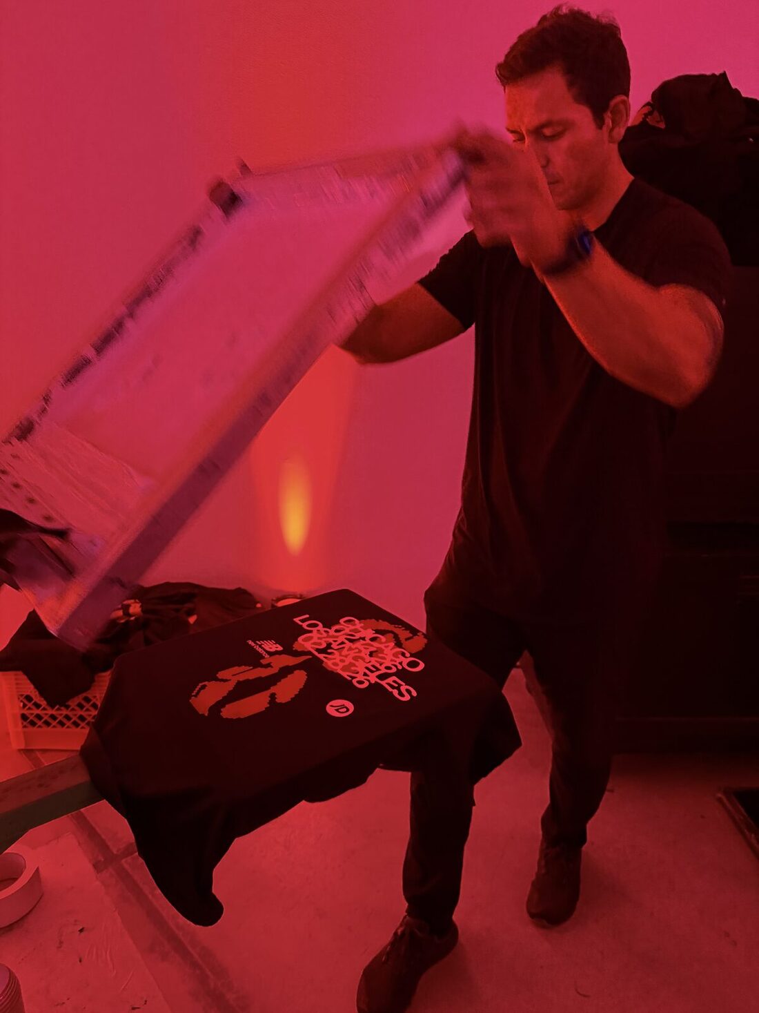 Printer lifting the screen off a freshly pulled black shirt under red event lighting