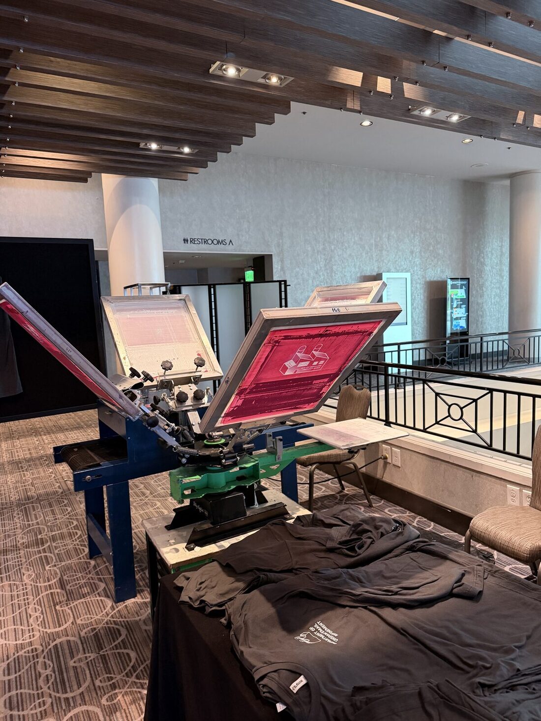 Four-color carousel screen-printing press with a loaded screen and folded printed shirts stacked beside it